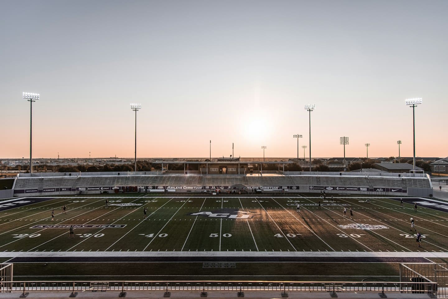 Empty American football stadium with players practicing on the field.