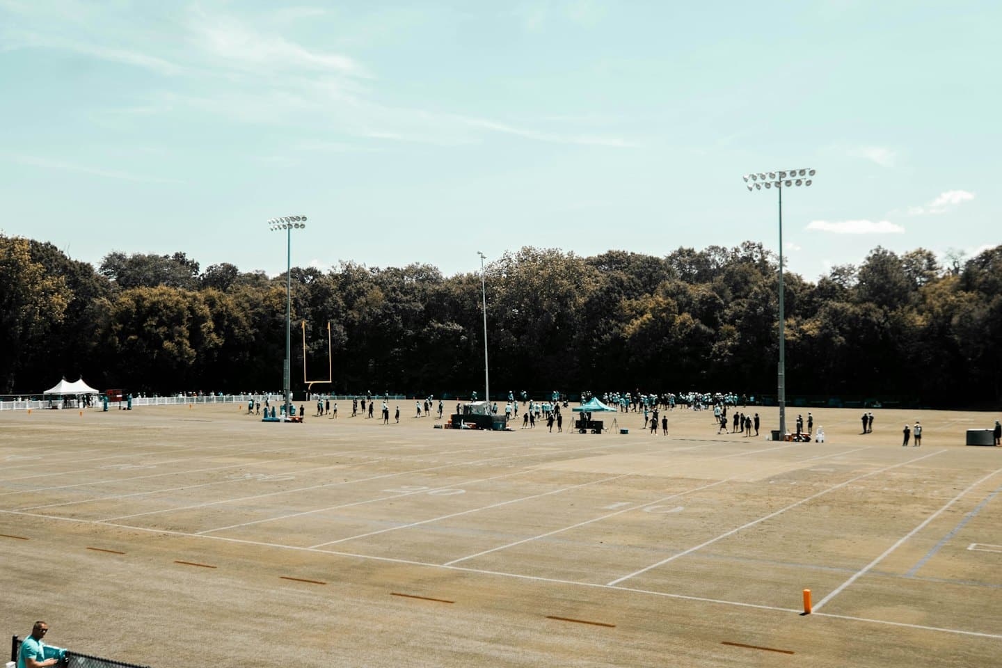 Athletes and staff practice on an expansive American football field.