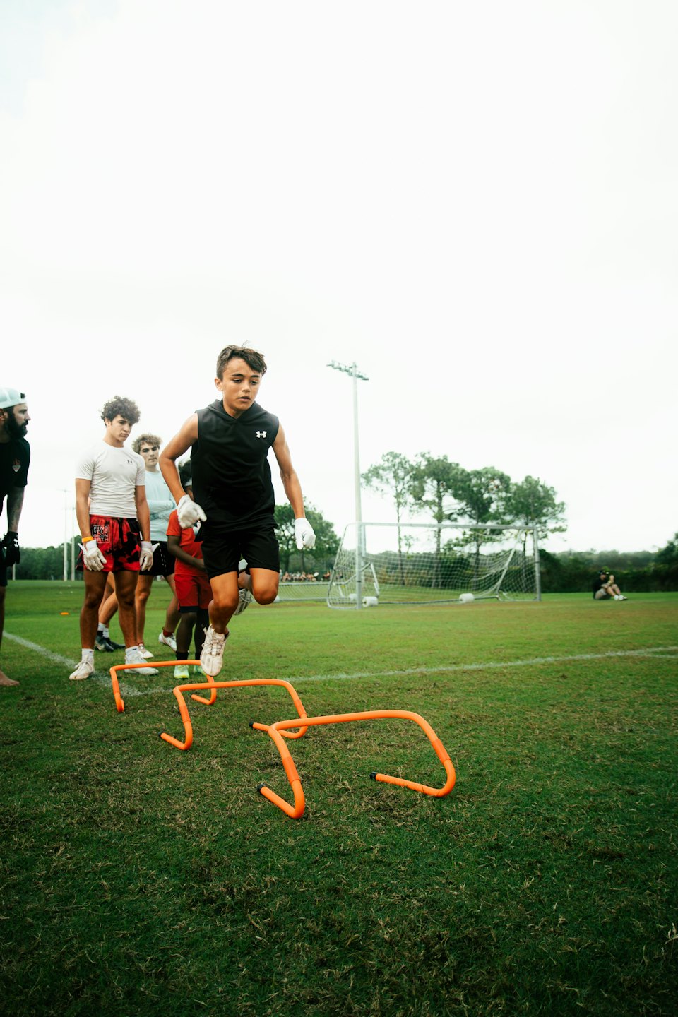 An athlete jumps over an orange hurdle on a grass field.