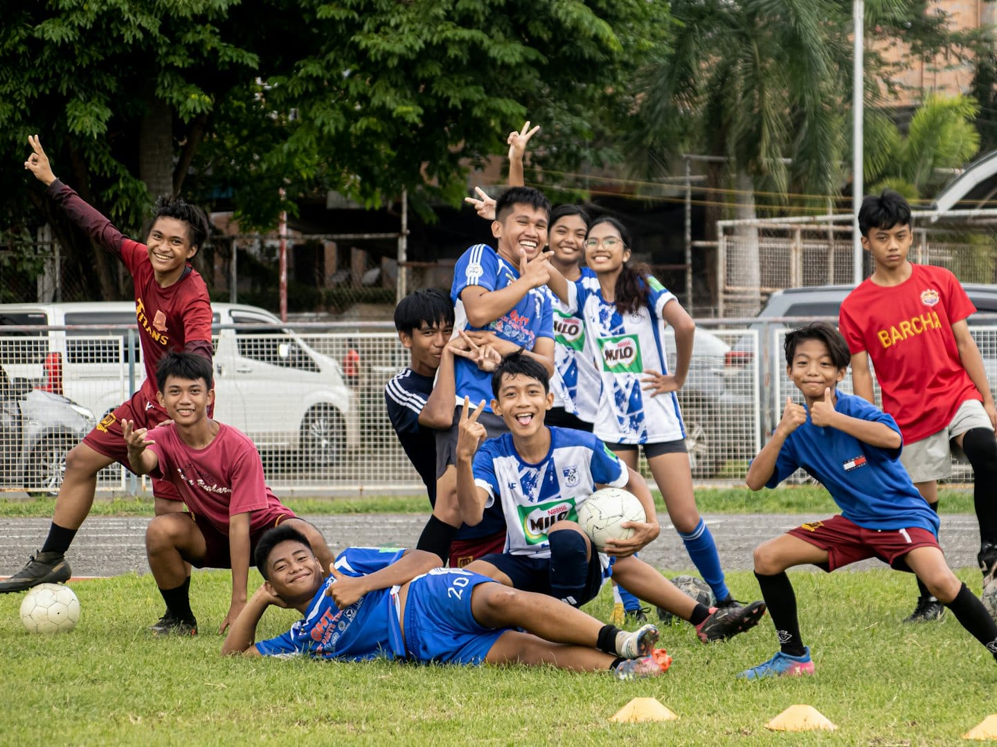 Teenagers in soccer uniforms making peace signs on a field.